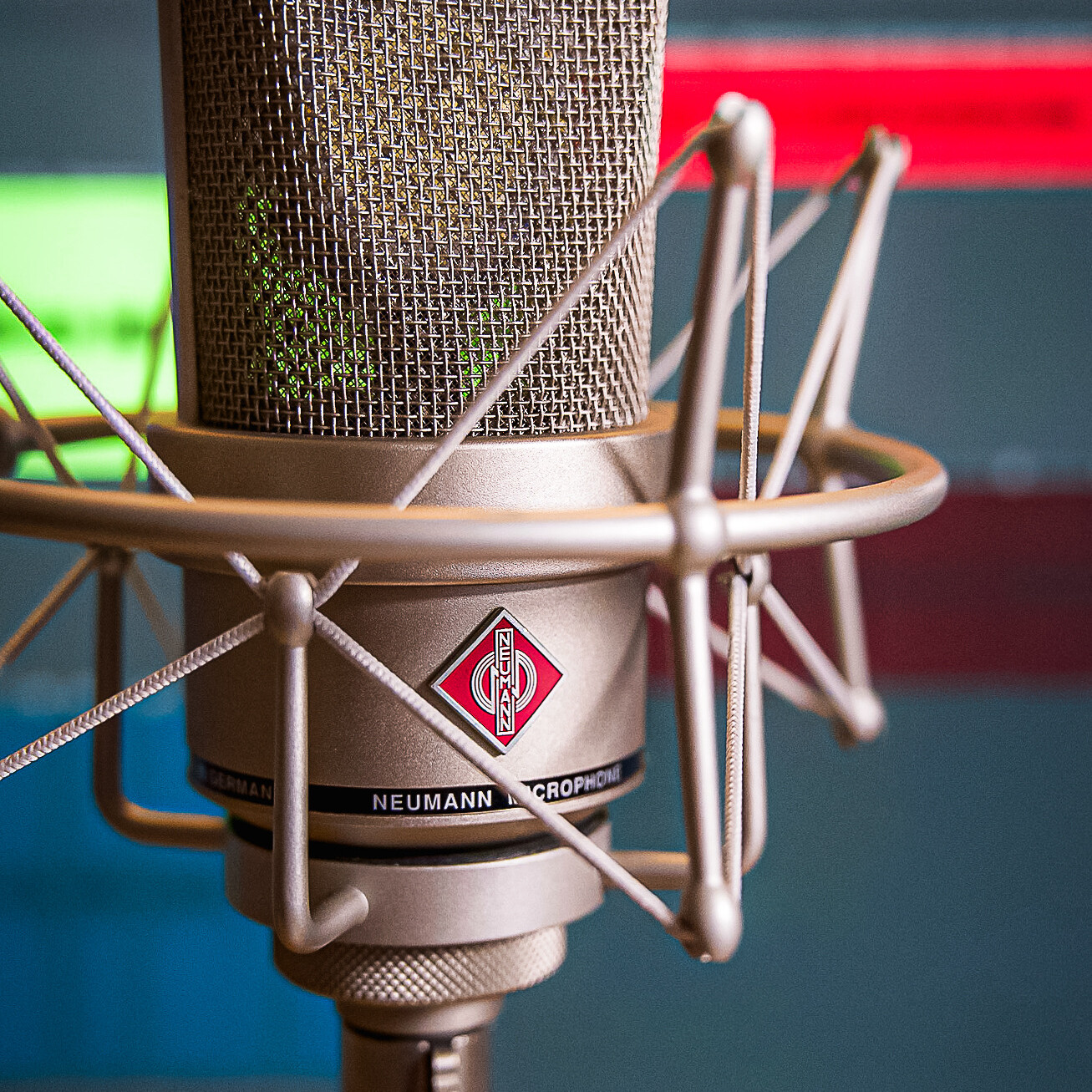 Neumann Gro&szlig;membran‑Mikrofon in Shockmount vor einer unscharfen Tonspur/DAW‑Wellenform im Hintergrund; Studioaufnahme f&uuml;r Podcast‑Produktionen.